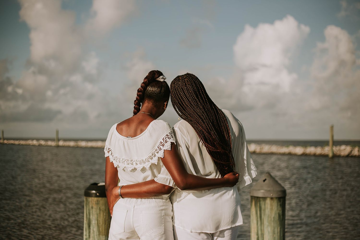 A couple embraces while overlooking a peaceful harbor from a wooden pier.