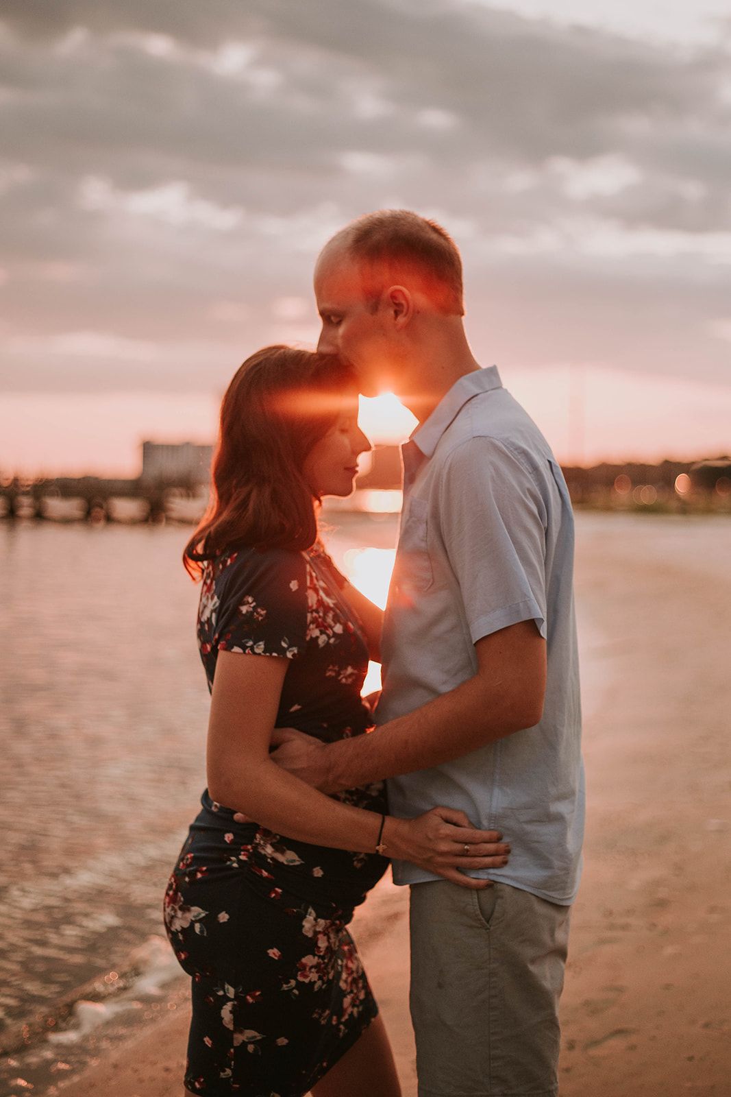 A romantic sunset silhouette of a couple embracing on a beach with a pier in the background.