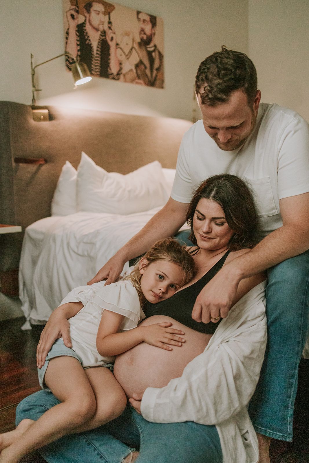 A family cuddles together on a bed while bonding with an expectant mother's pregnant belly.