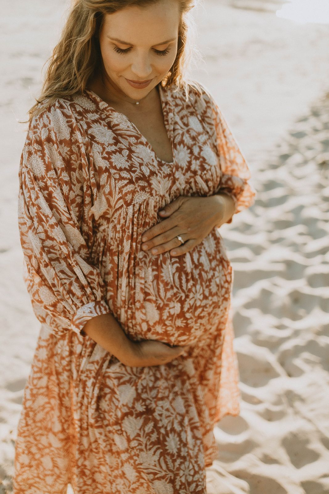 Maternity beach photo featuring floral printed dress in warm sunset lighting.