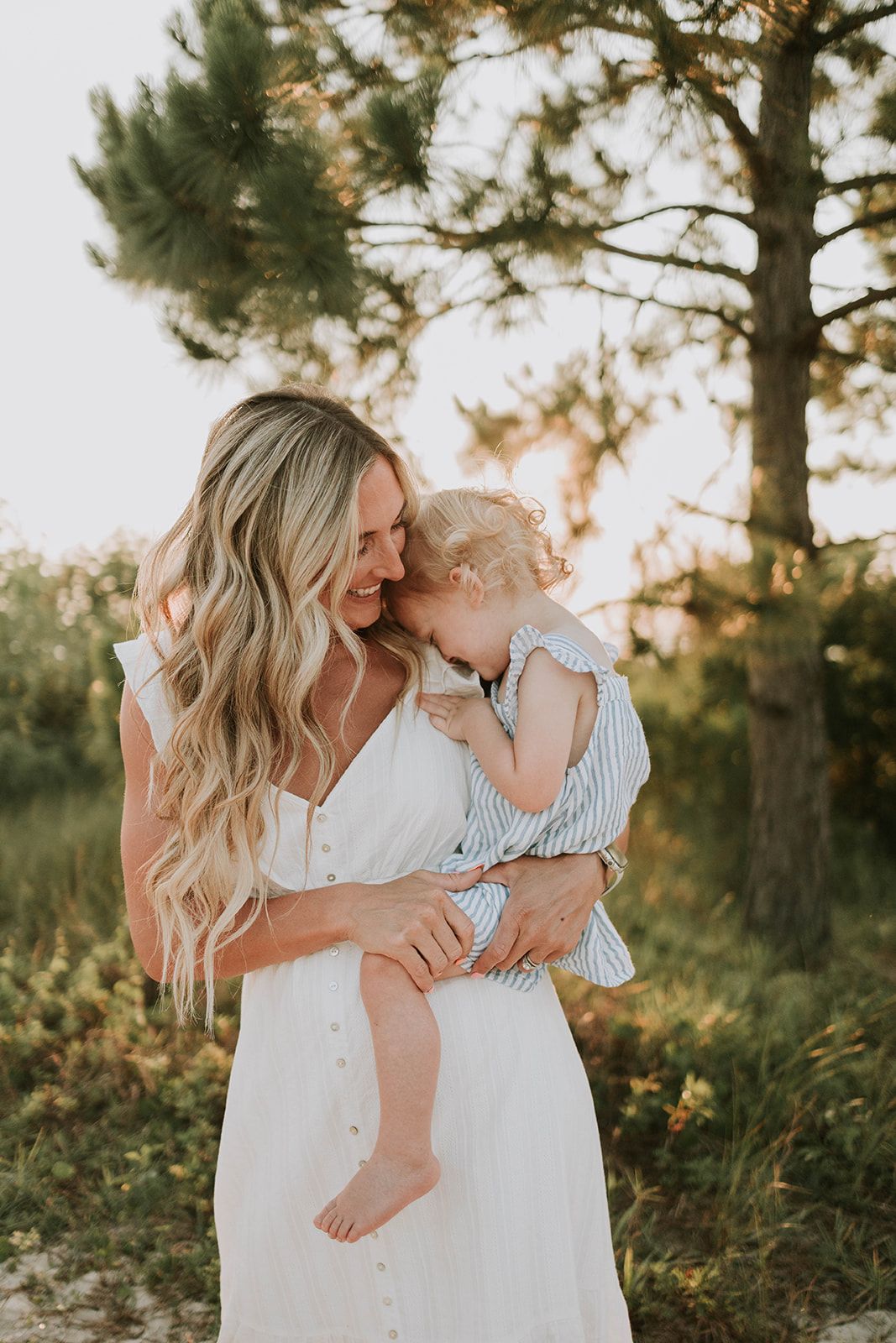 A tender moment captured during a sunset photoshoot outdoors with golden light filtering through pine trees.