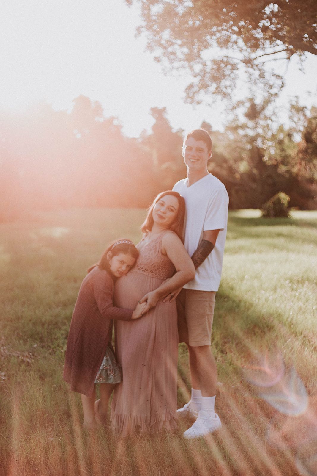 A family shares a tender moment in a sunlit field during golden hour.