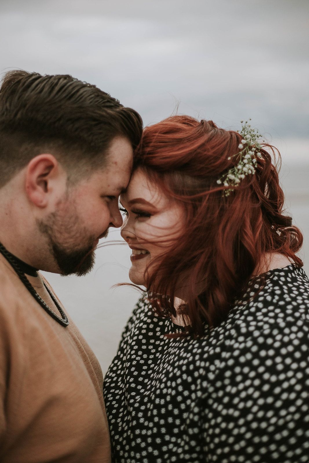 A romantic close-up portrait showing intimate connection against an overcast sky.