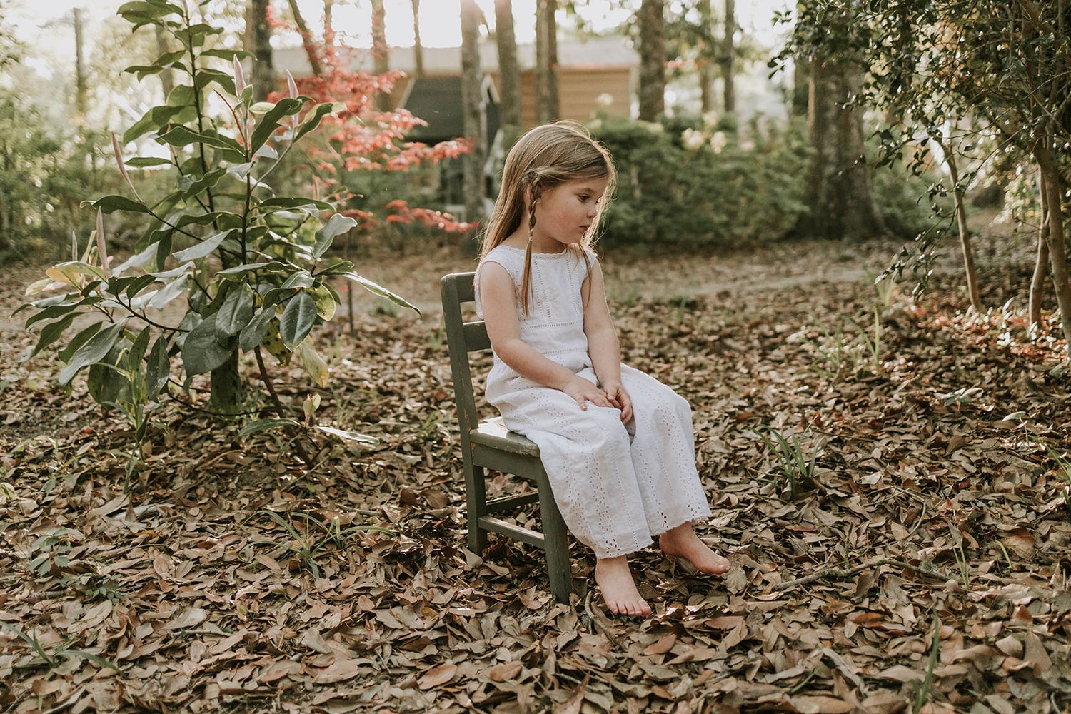 A child in white clothing sits thoughtfully on a wooden swing surrounded by fallen leaves.
