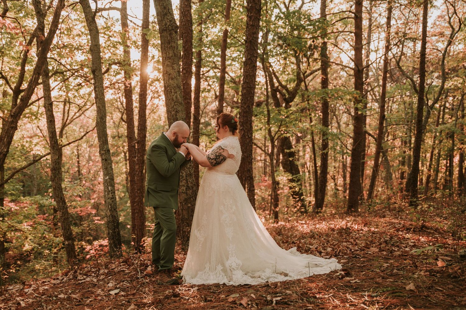 A romantic autumn wedding photo captured in a sunlit forest with fallen leaves and warm golden lighting.