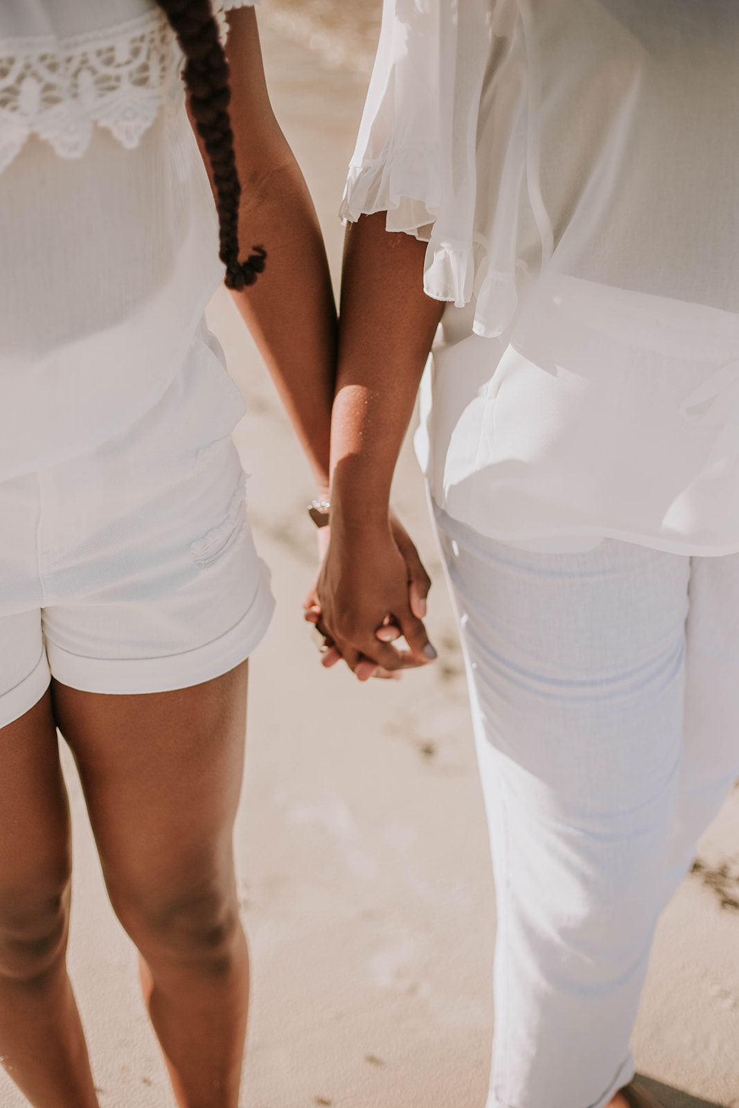 Two people holding hands while wearing white clothing on a sunny beach.