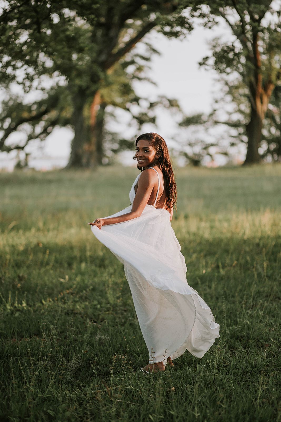 Woman in a flowing white dress twirls in a sunlit meadow.