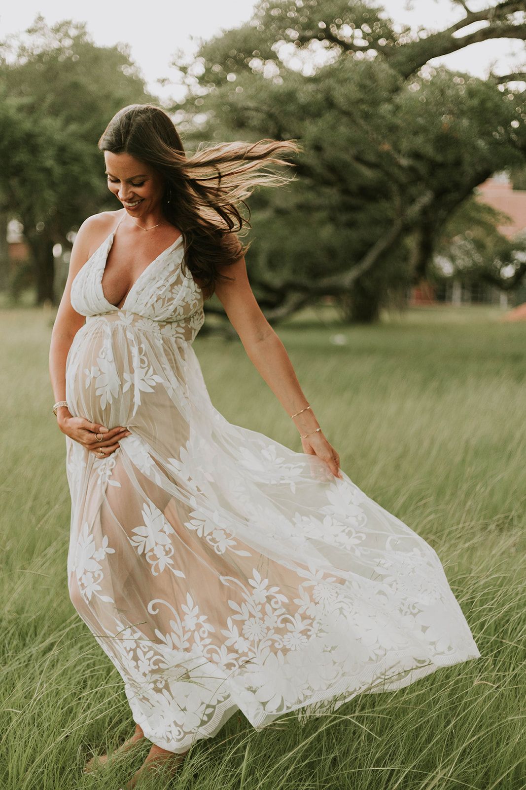 Flowing white lace maternity dress catches breeze in sunlit field.