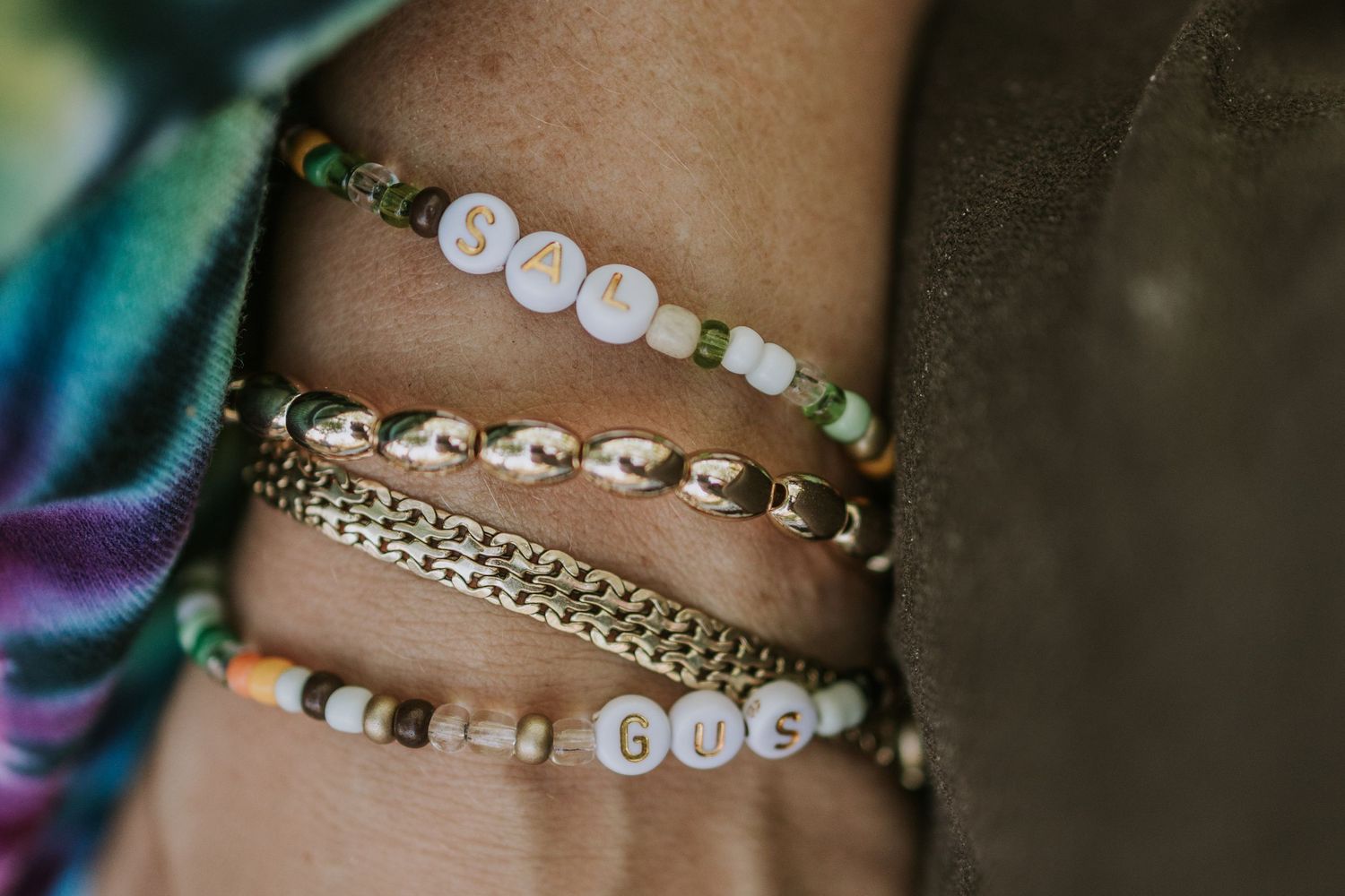 Stack of beaded bracelets featuring white lettered beads and crystal chains on colorful iridescent fabric.