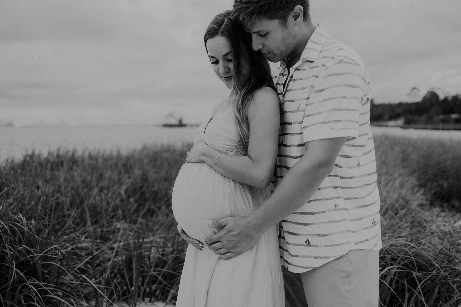 Black and white portrait of couple sharing intimate moment on coastal grassland.