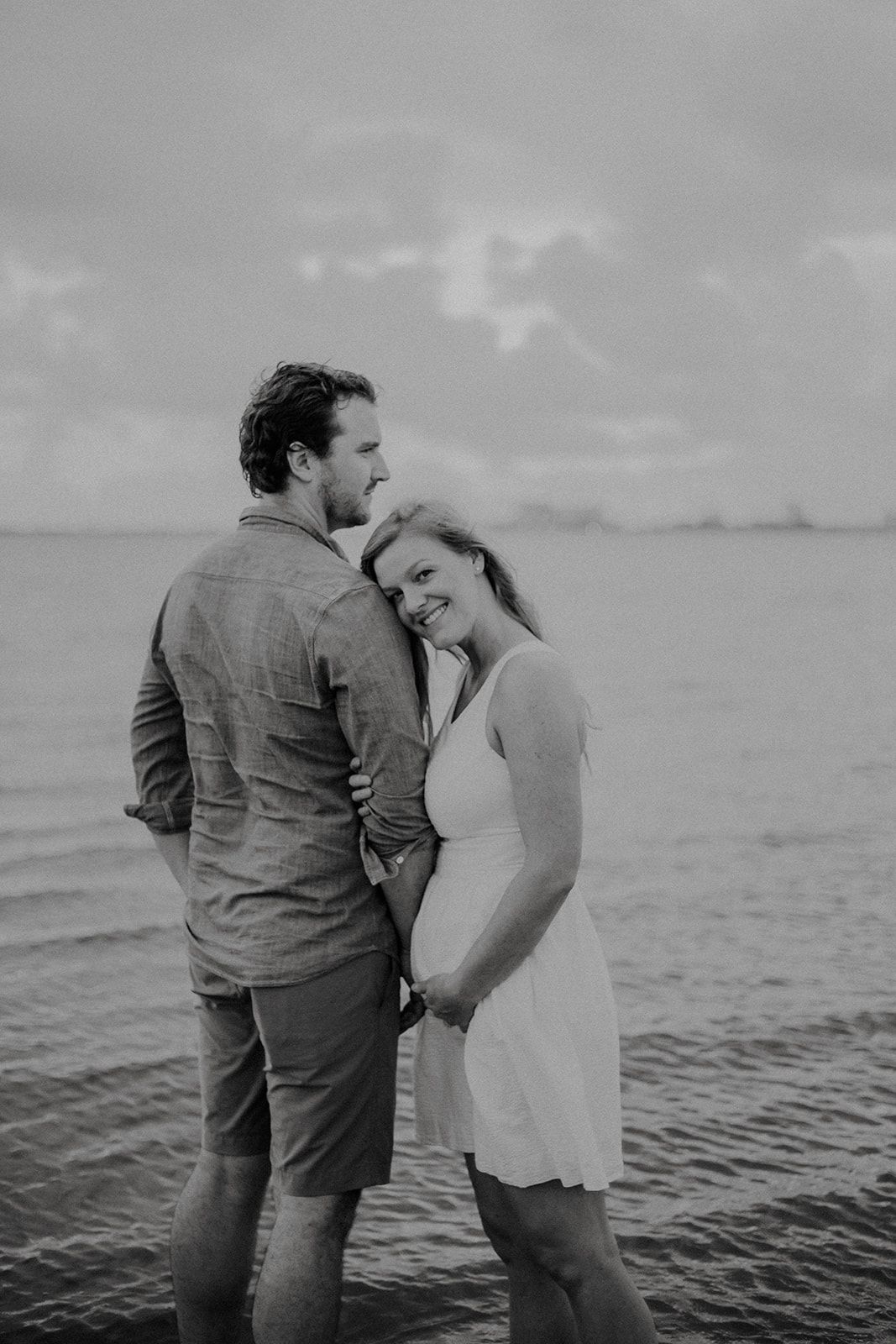 A black and white beach portrait capturing a tender moment with ocean waves in background.