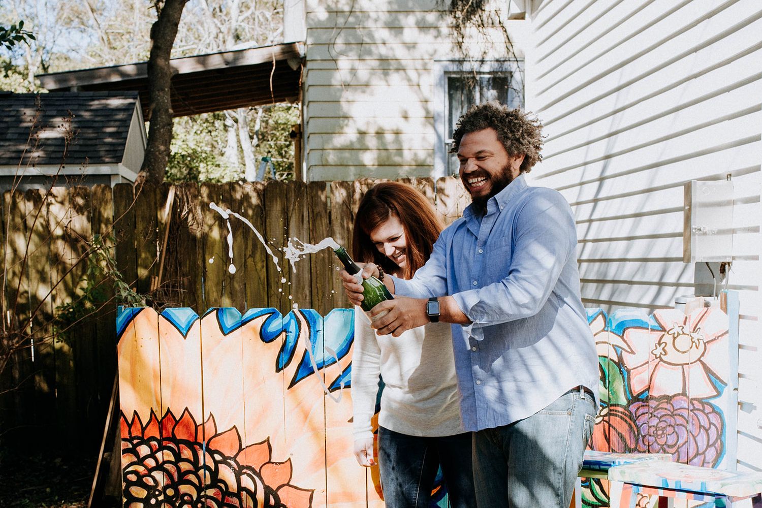 Two people painting a colorful mural together on an outdoor wall in bright daylight.