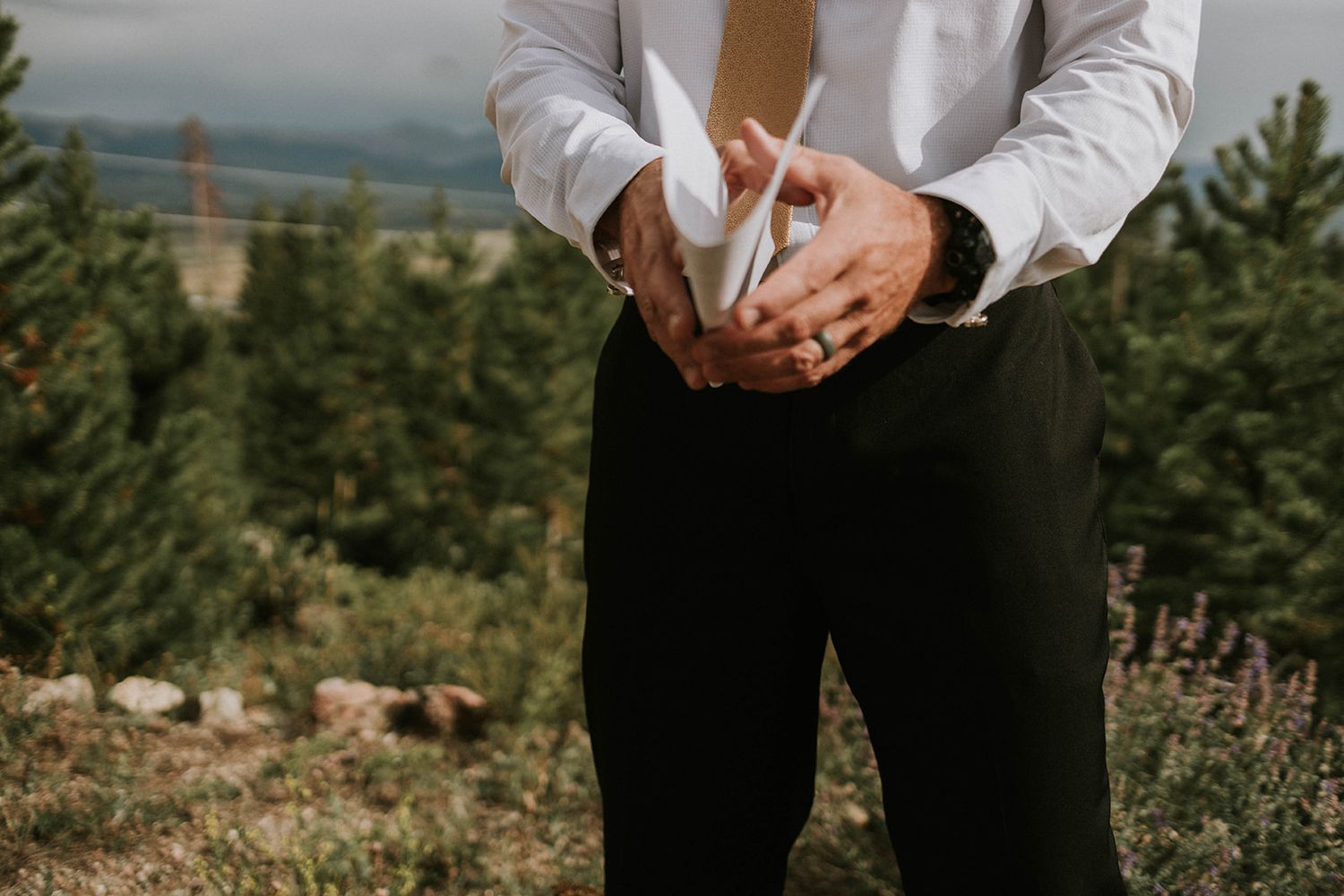 Close-up view of hands adjusting formal white dress shirt sleeves against scenic mountain landscape background.