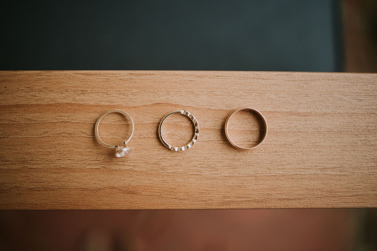 Three elegant gold rings displayed on a wooden surface, including a pearl ring, beaded band, and plain band.