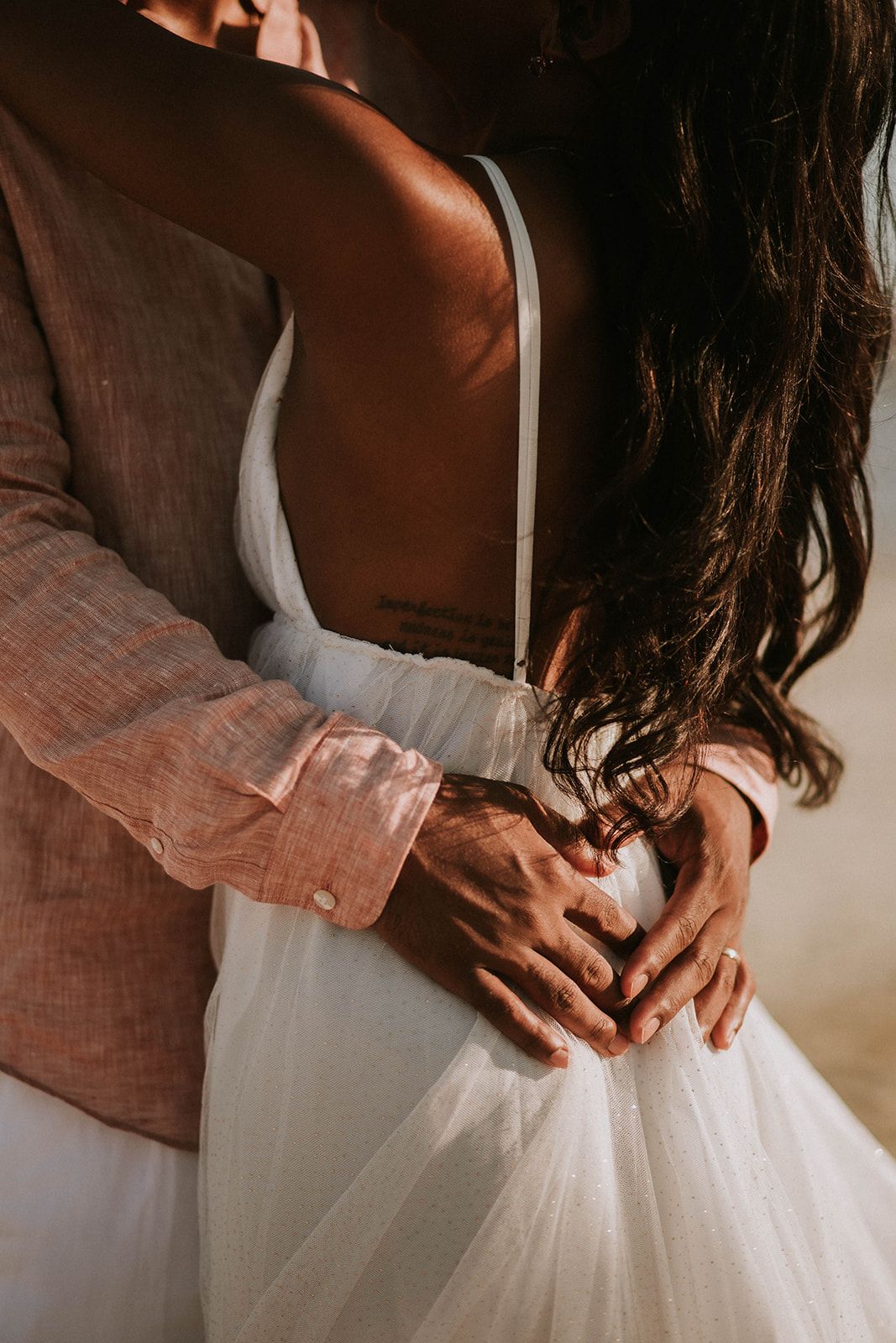 Intimate close-up of hands fastening a white wedding dress with delicate tulle fabric.