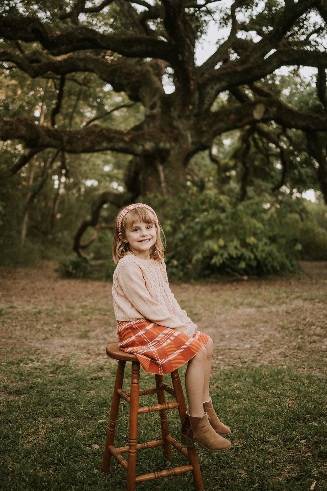 Photography session under a large oak tree with brown wooden stool and soft earth tones in natural outdoor setting.