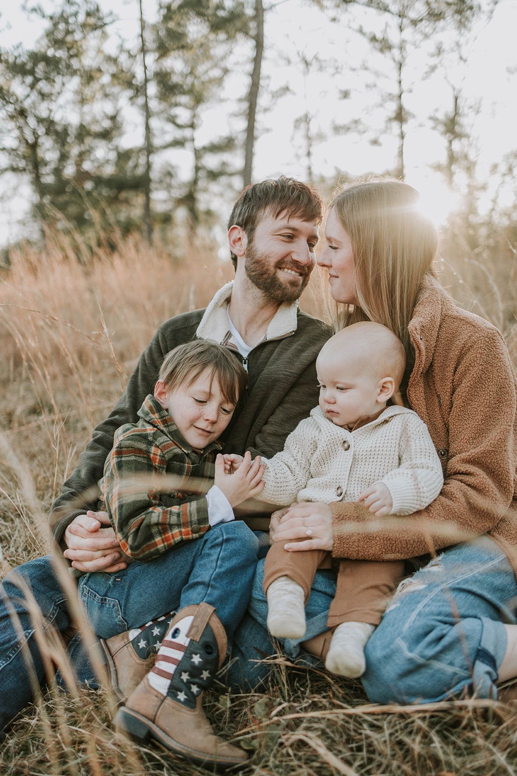 Family sharing intimate moment together in tall grass during sunset.