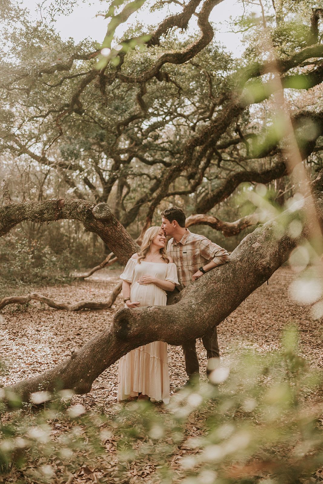 Couple sitting on large tree branch in dreamy forest setting.