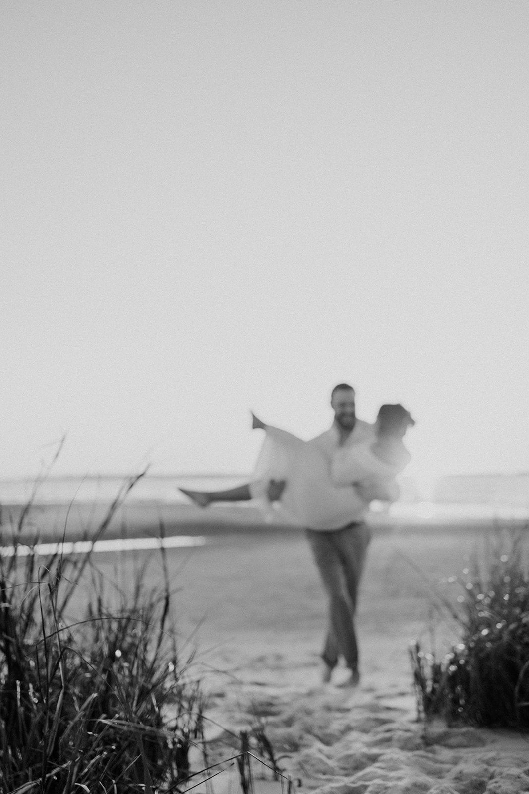 A black and white artistic beach photo captures a joyful moment of movement and celebration at sunset.