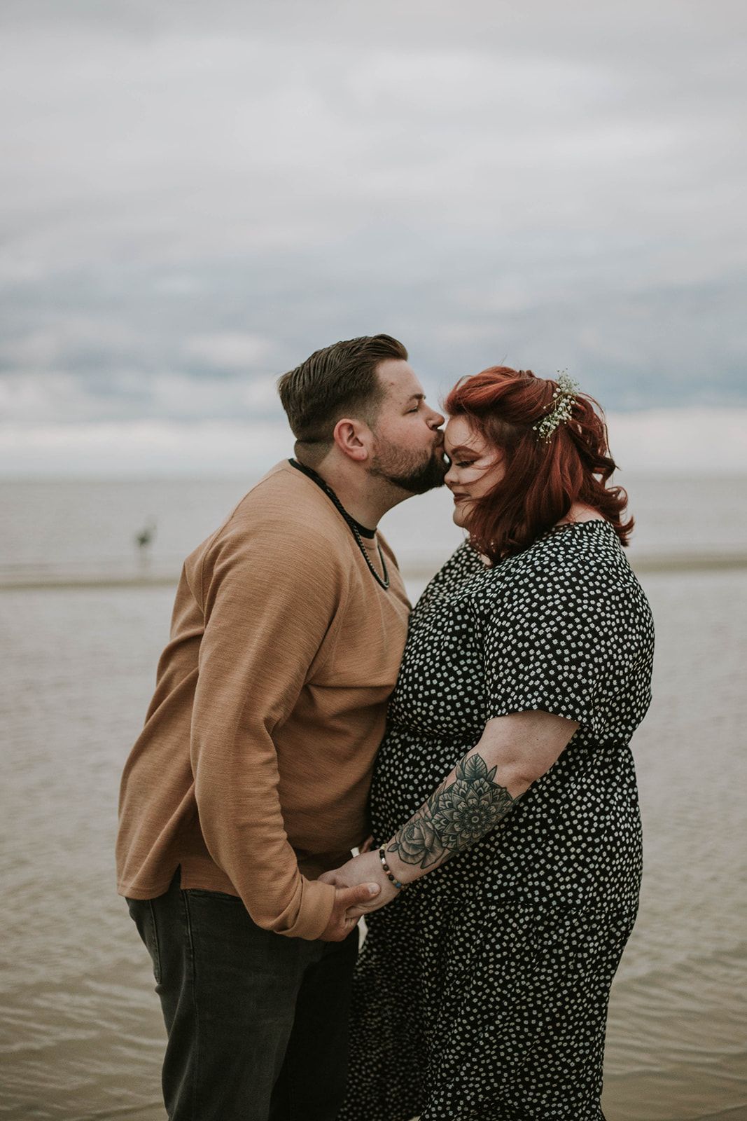 A romantic beach portrait showing tender affection against cloudy coastal backdrop.