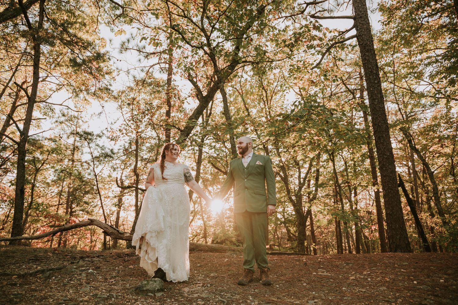 A couple strolls through a sun-drenched autumn forest with warm golden light filtering through the trees.