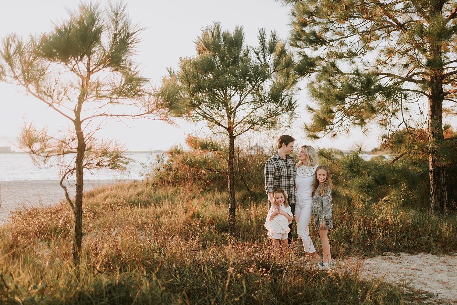 Family standing among pine trees at sunset near coastline.