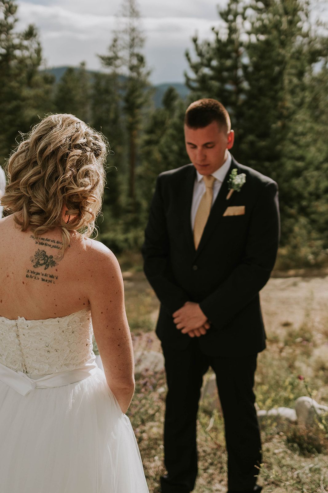 An intimate outdoor wedding scene set among evergreen trees in a mountain setting.