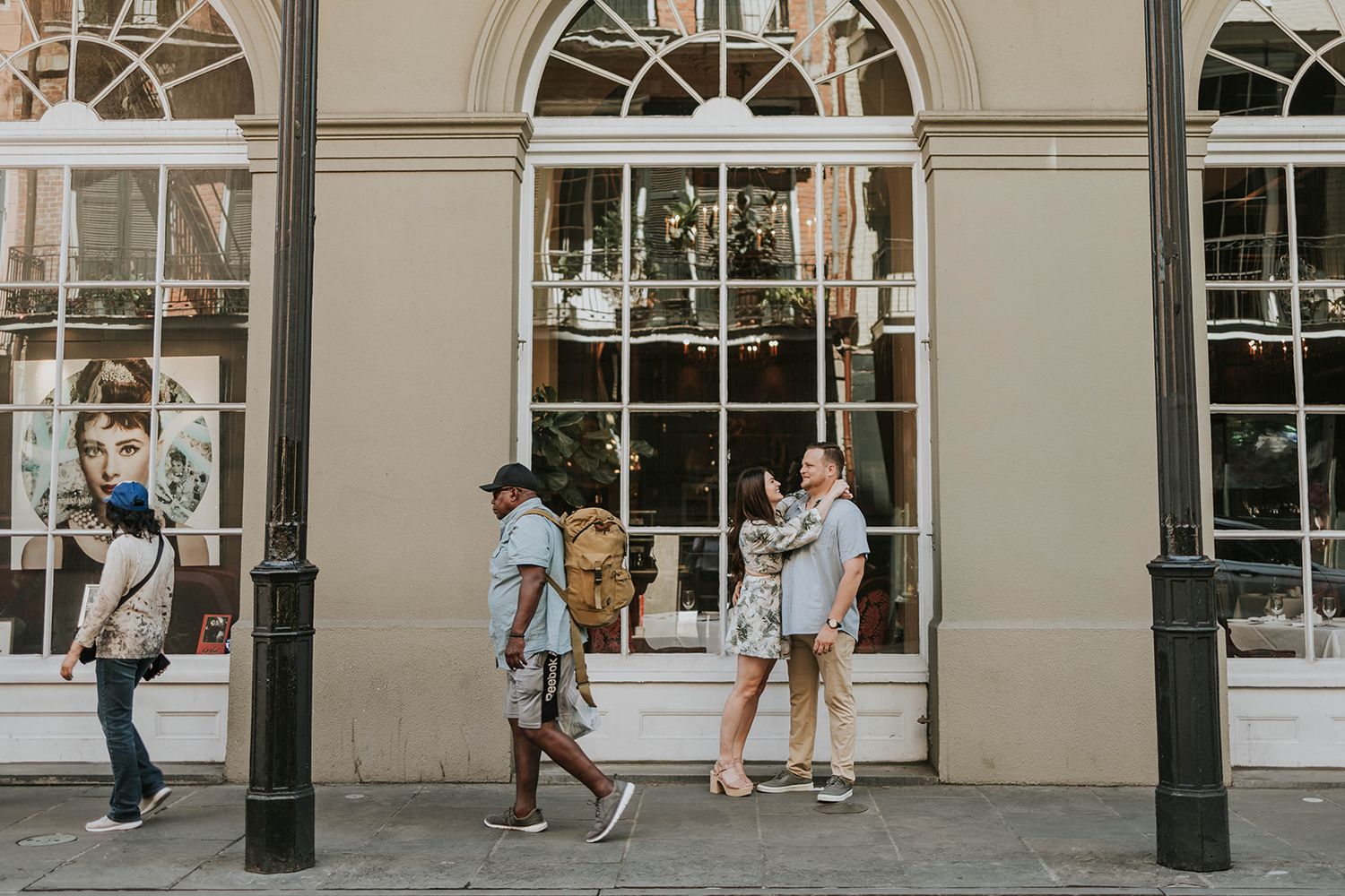 People walking past a historic building with arched windows and classical architecture.