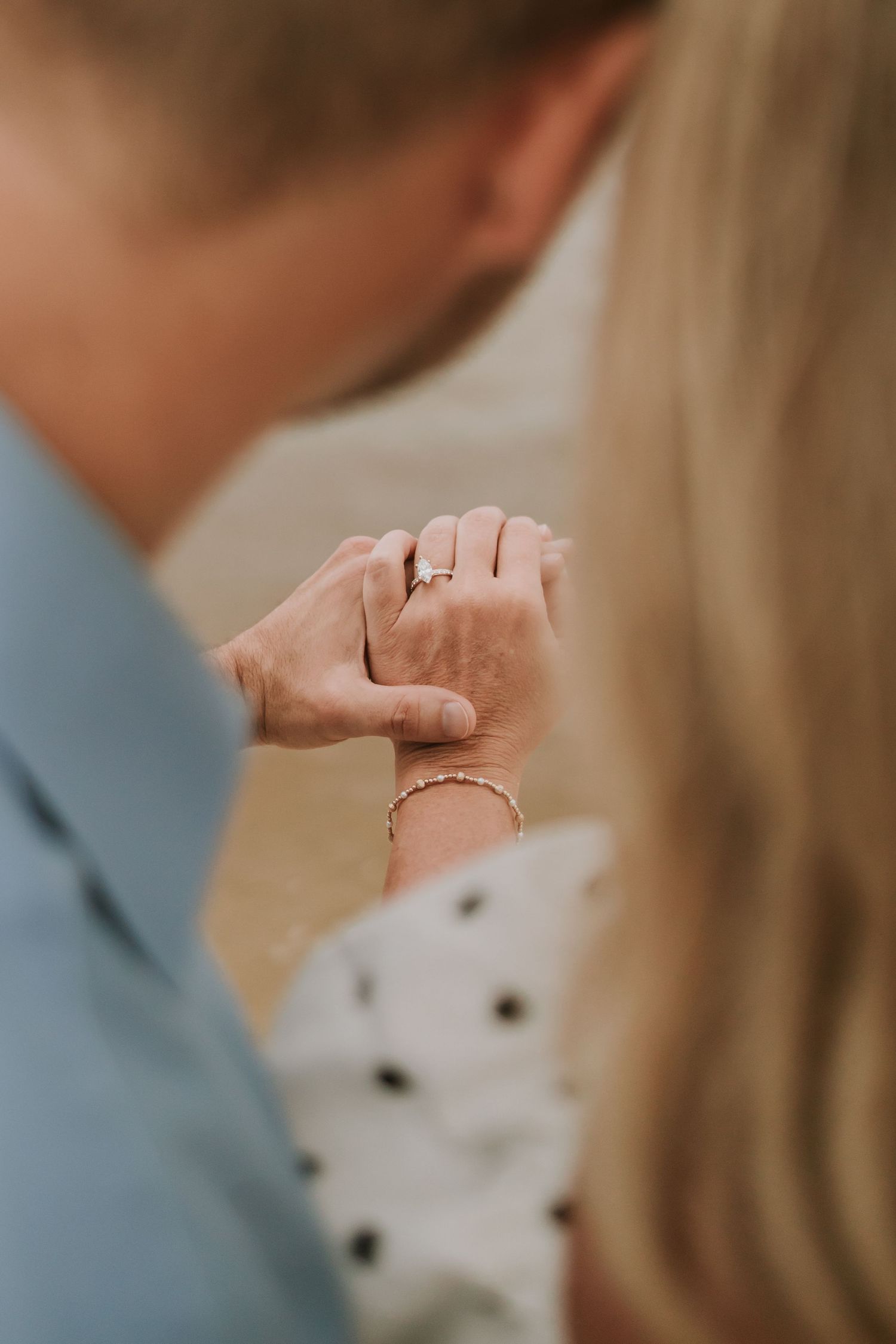 Close-up of couple holding hands, woman wearing diamond engagement ring and gold bracelet.