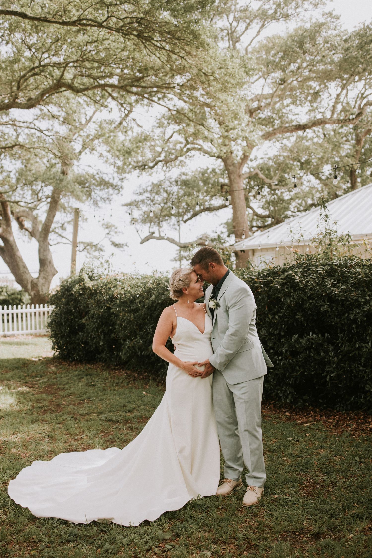 Bride and groom share a romantic embrace in a lush garden setting, bride wearing a flowing white gown with a long train.