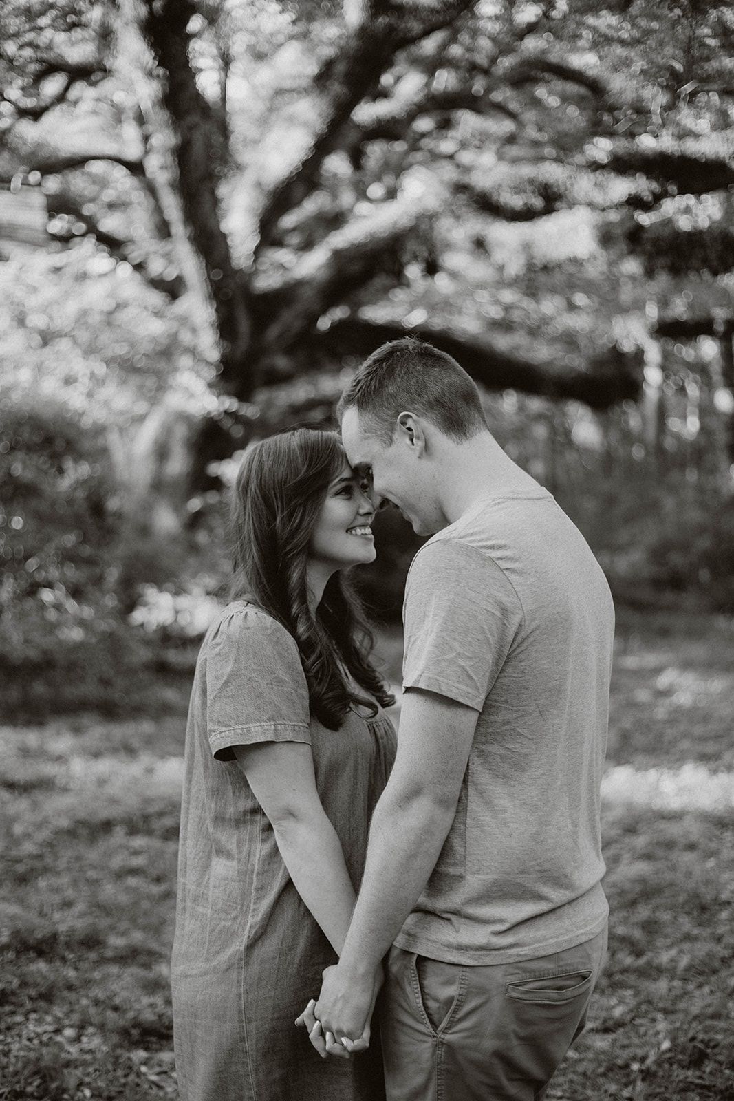 An intimate black and white portrait of a couple sharing a tender moment under a tree.