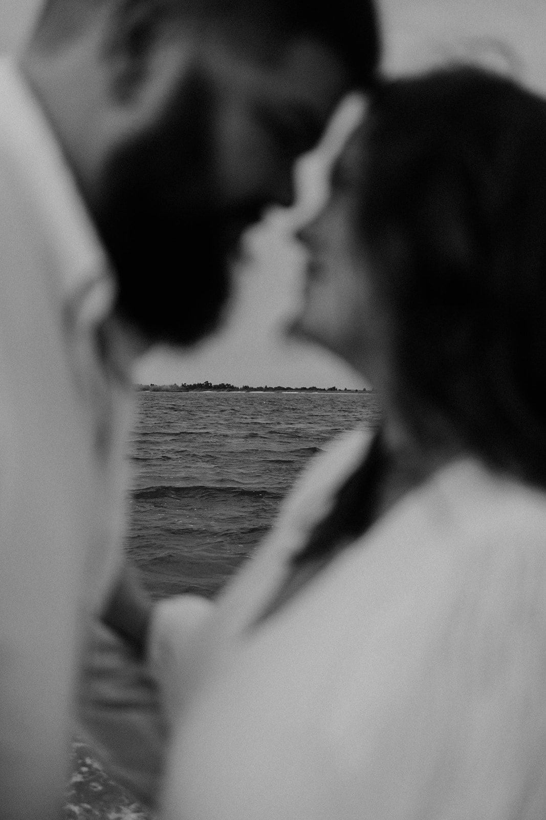 An intimate black and white photo of a couple with ocean waves in the background.
