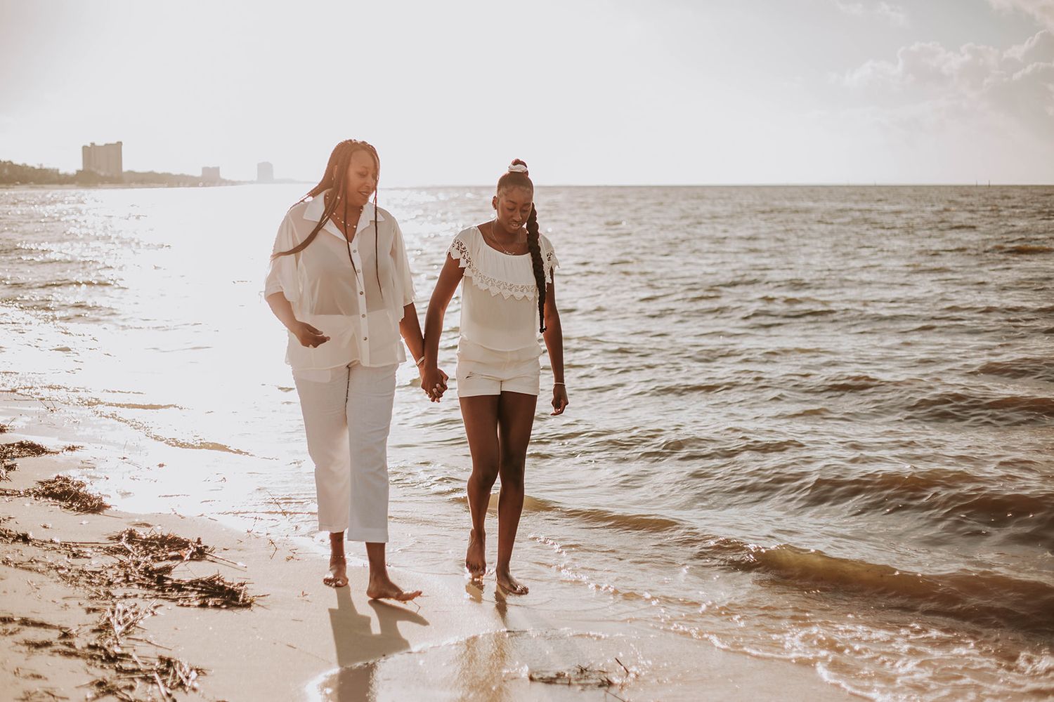Two people in white outfits walking together along a sunny beach shoreline.