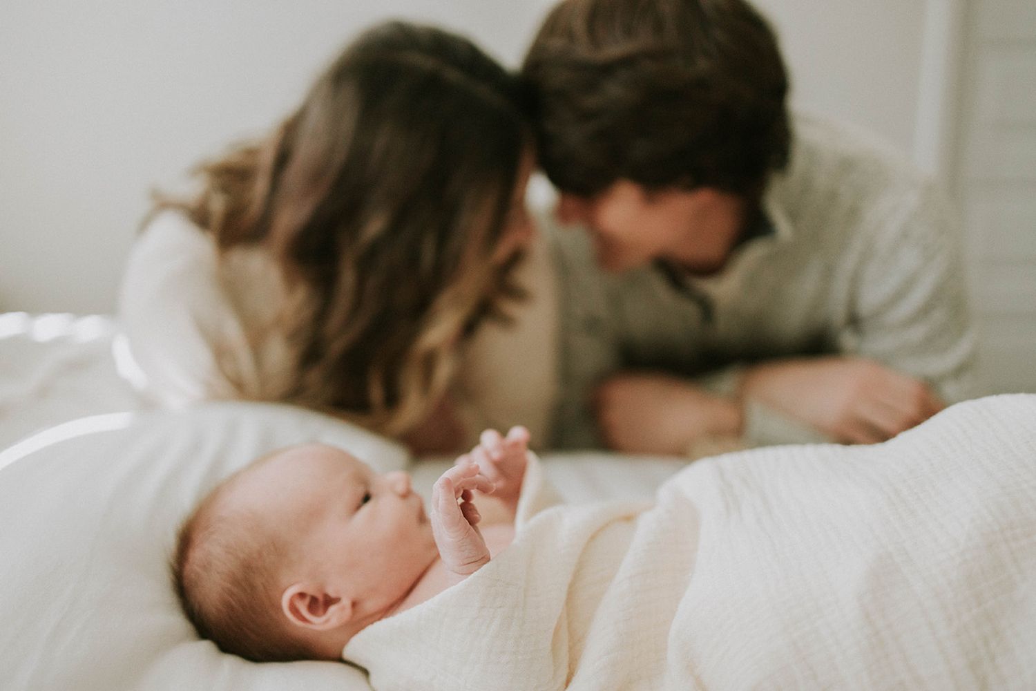 Peaceful moment with sleeping infant on white bedding while others look on.