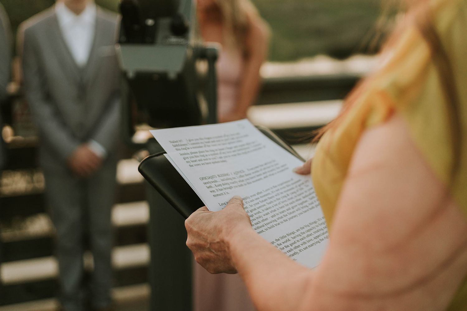 Wedding officiant holds ceremony notes while couple stands during an intimate outdoor ceremony.
