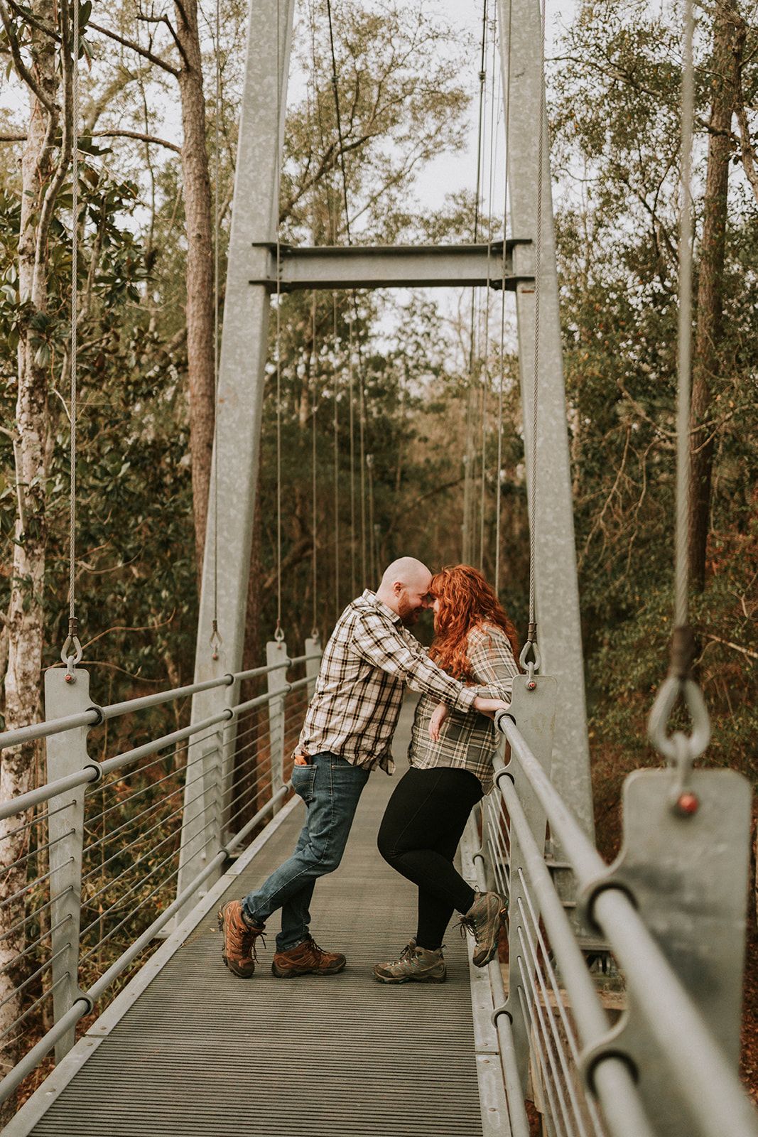 A playful couple sharing a romantic moment on a suspension bridge surrounded by trees.