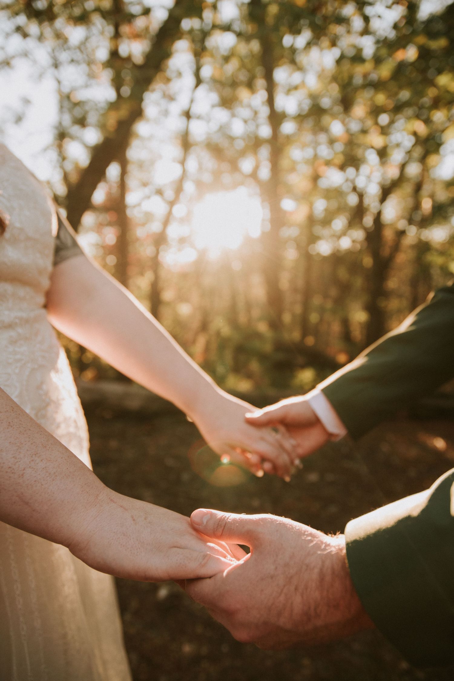 Two people holding hands in a forest at sunset with golden light filtering through the trees.