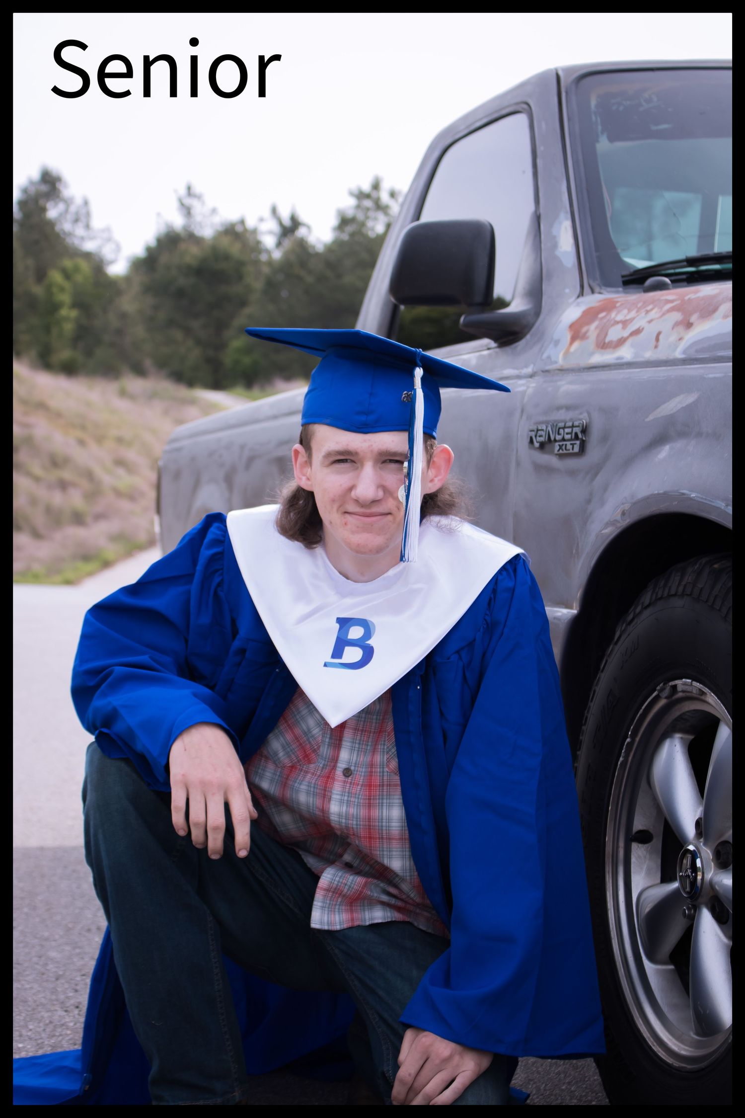high school boy wearing cap and gown in front of truck