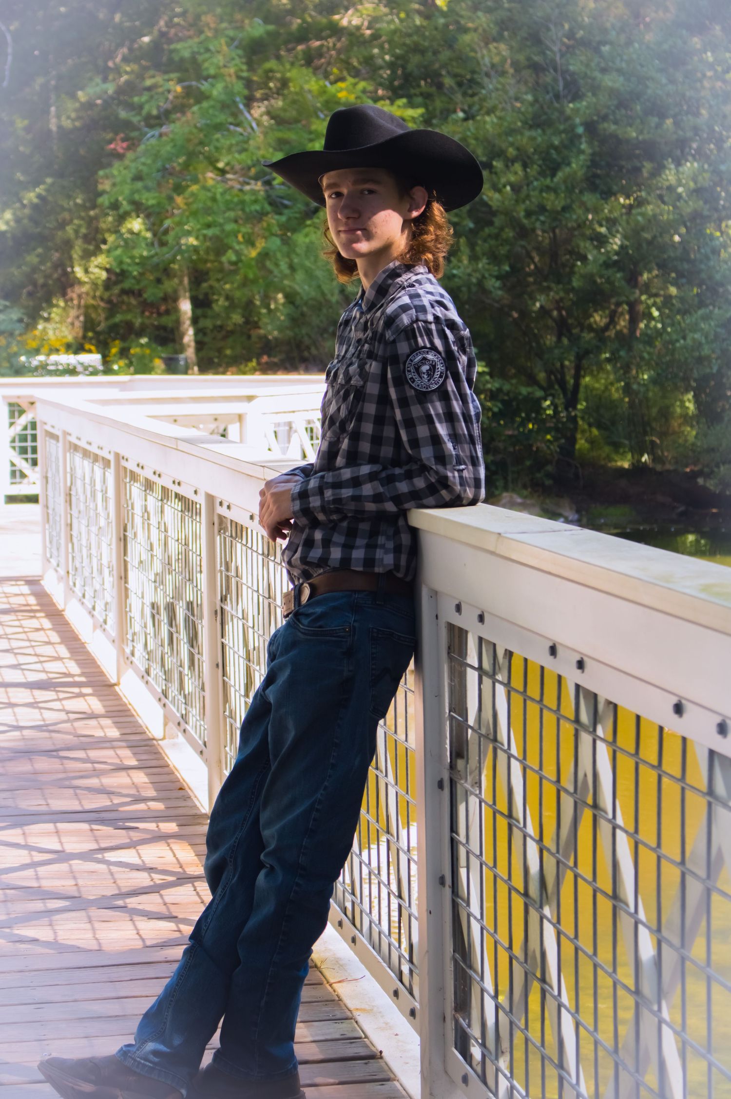 young man with cowboy hat on propped against a bridge rail