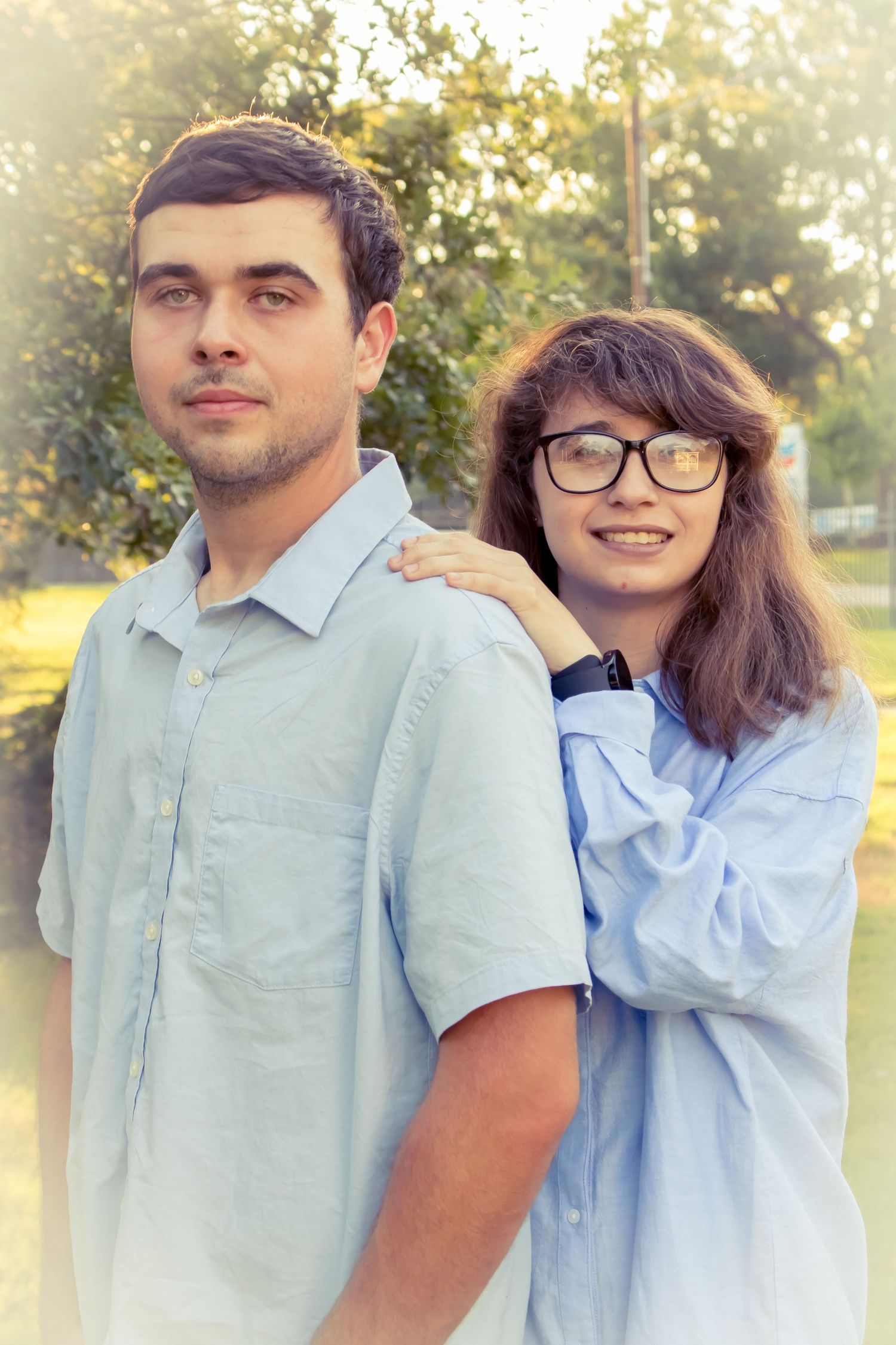 Woman standing behind man, gently holding his shoulders during outdoor photo session