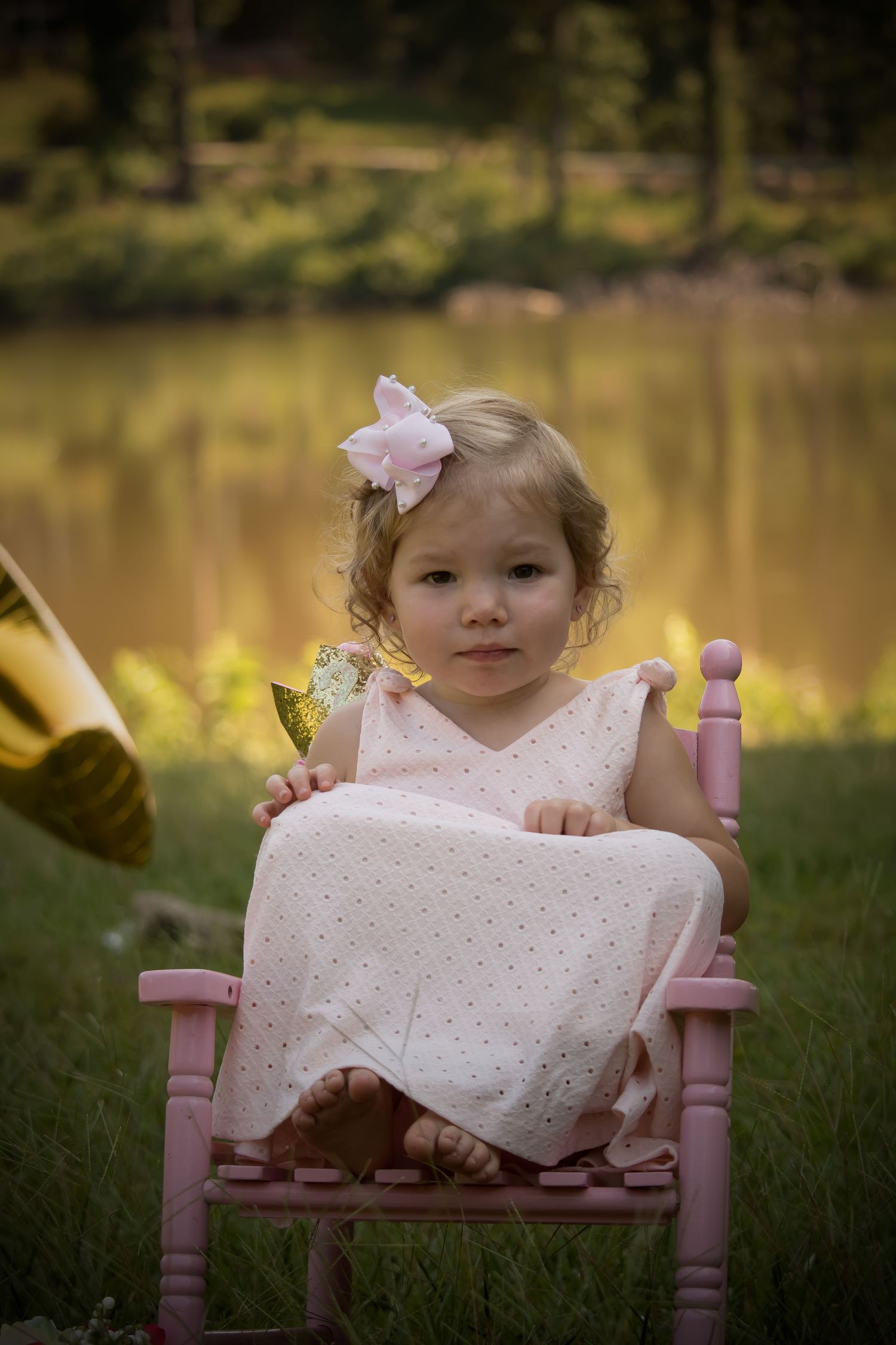 Toddler sitting in pink chair near lakeside in natural light portrait