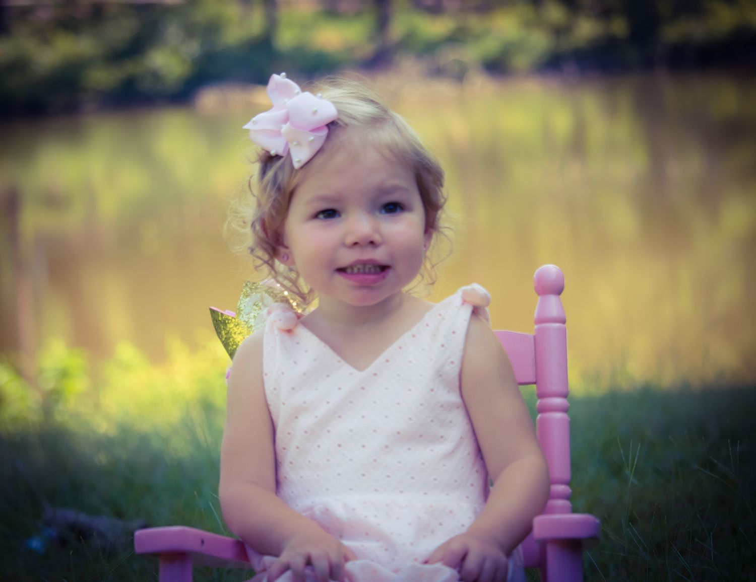 Toddler sitting in pink chair near lakeside in natural light portrait