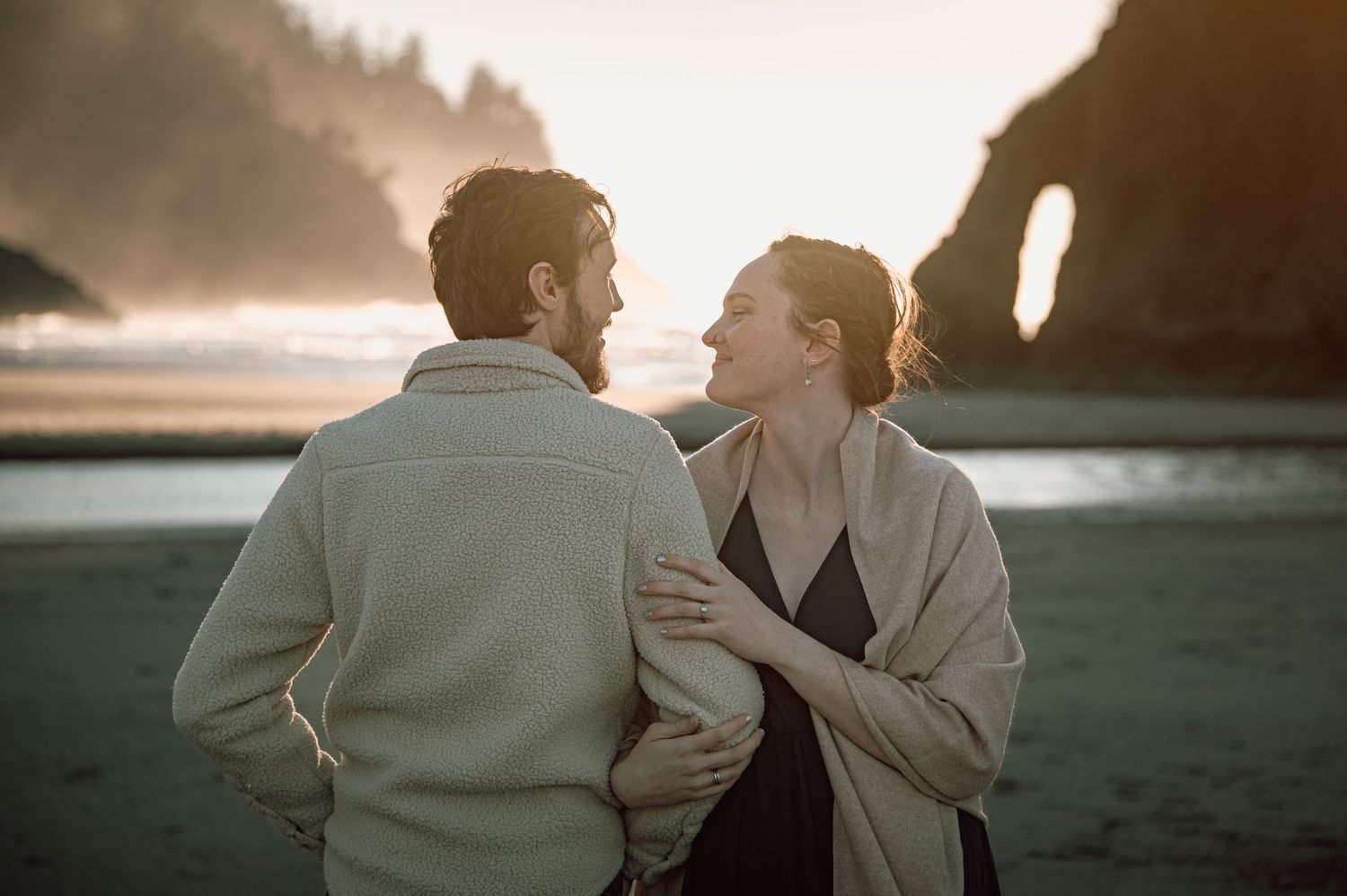 Couple sharing a romantic moment on a misty beach at sunset with sea stacks in the background.