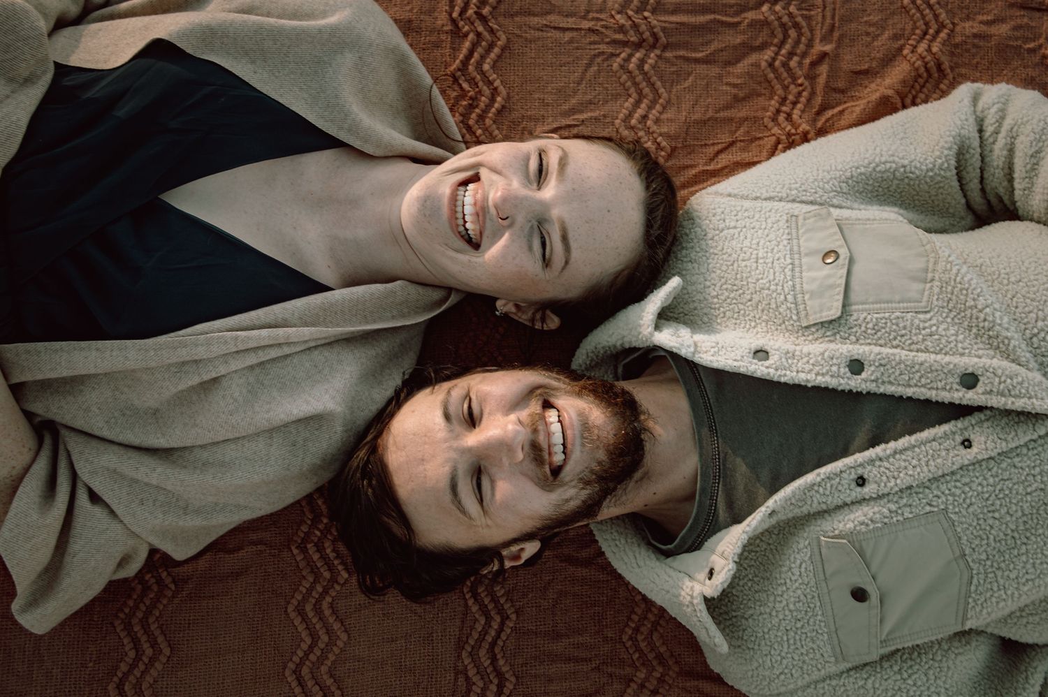 Laughing couple lying on floor looking up joyfully.