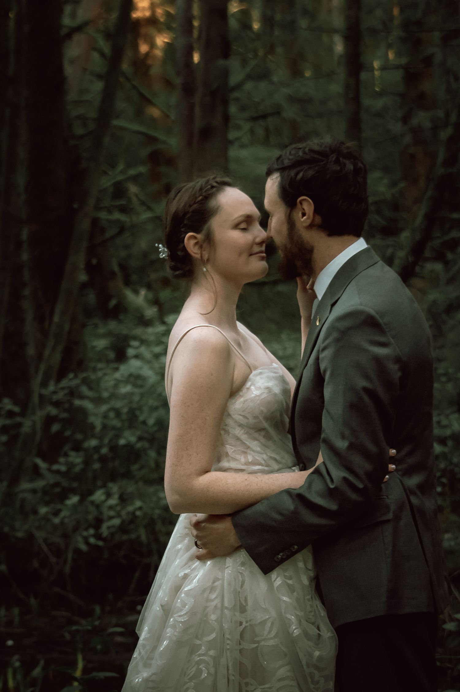Bride and groom share a romantic kiss in a lush green forest during their wedding day.