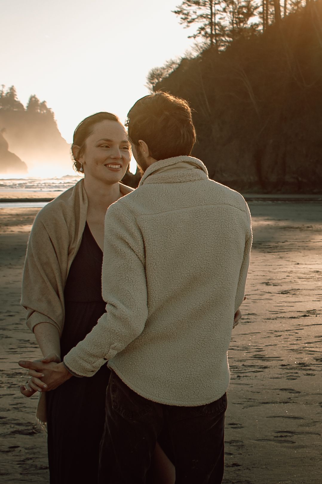 Smiling woman embracing man on sandy beach at golden sunset.