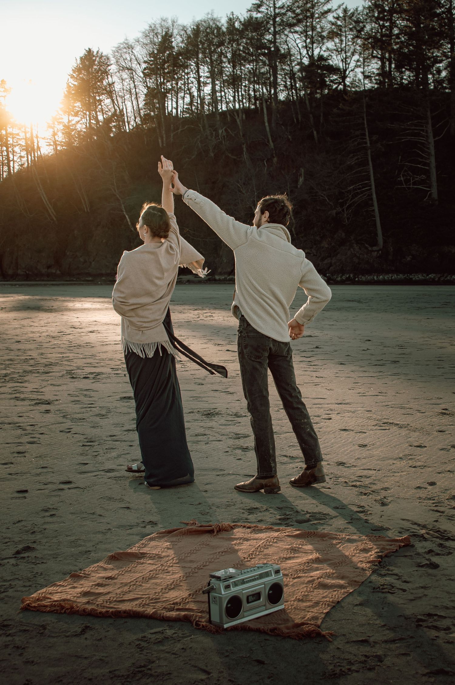 Couple dancing on beach at sunset with vintage boombox on blanket.