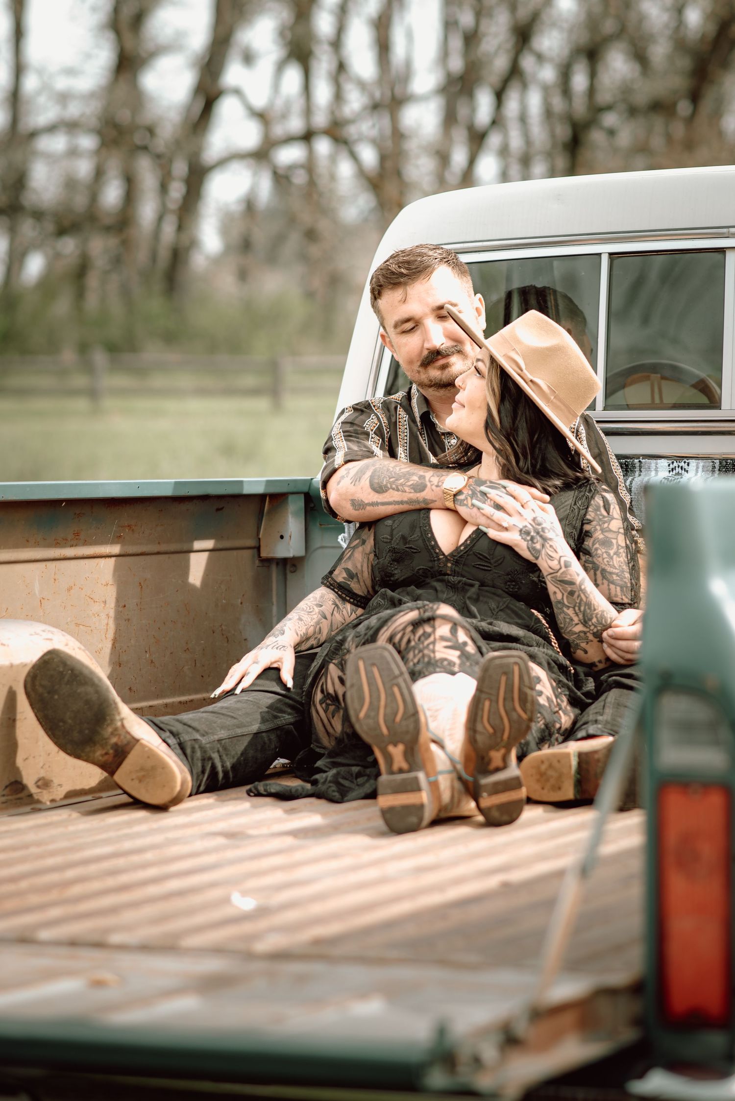 Tattooed couple relaxing in the bed of a vintage teal pickup truck in a rural setting.