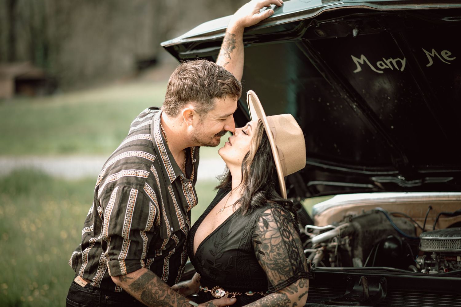 Couple kissing passionately in front of a vintage truck hood with Marry Me written inside it.