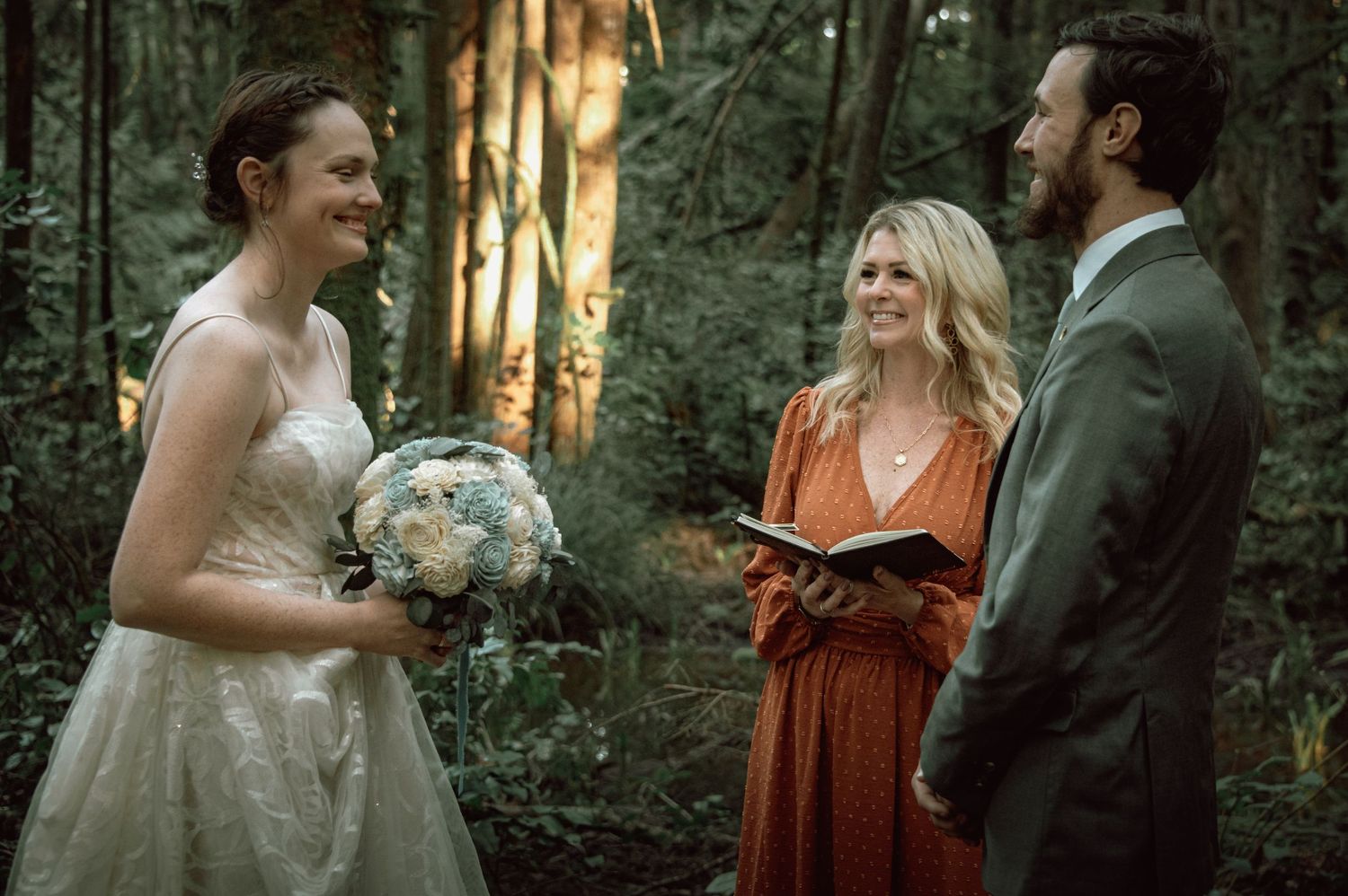 Bride and groom exchange vows with officiant in a lush forest wedding ceremony.